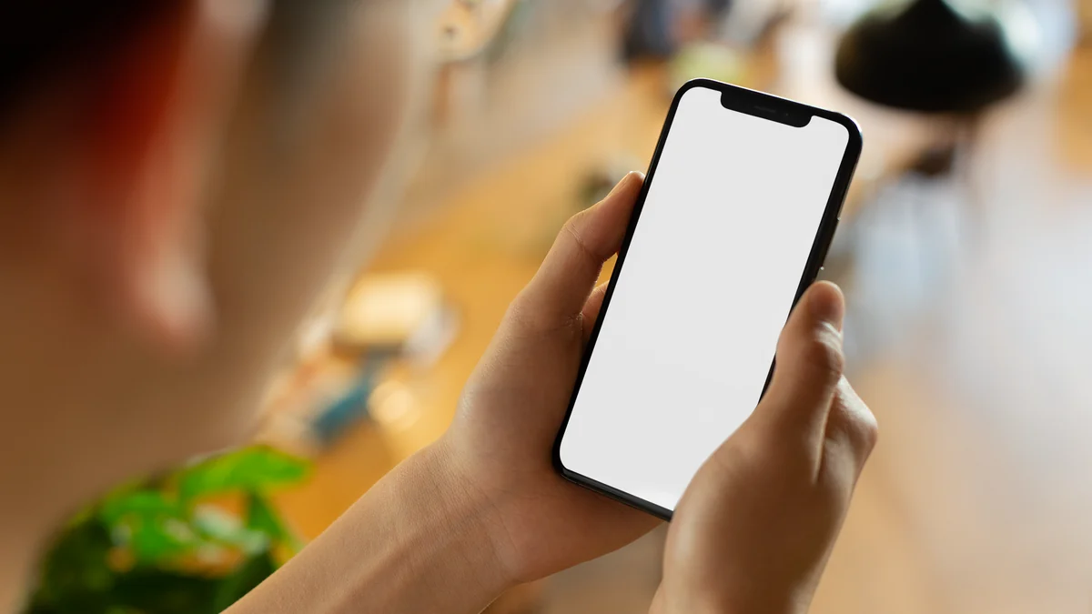 Over the shoulder view of someone holding a phone with a completely blank white screen, in a warm cafe